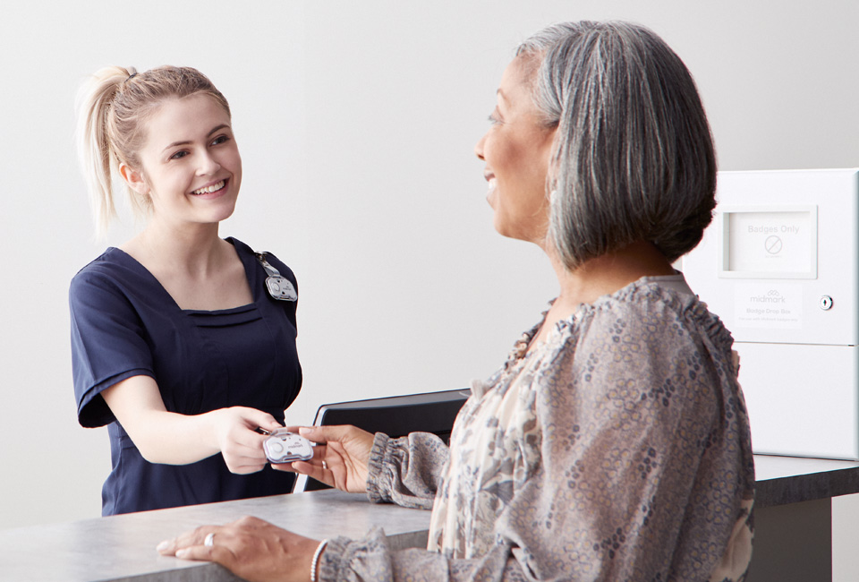 Staff handing a patient their Midmark RTLS badge over a counter