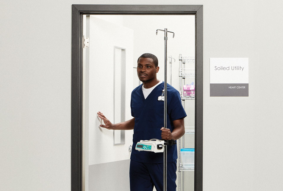 Nurse walking out of a room with a biomed IV pump