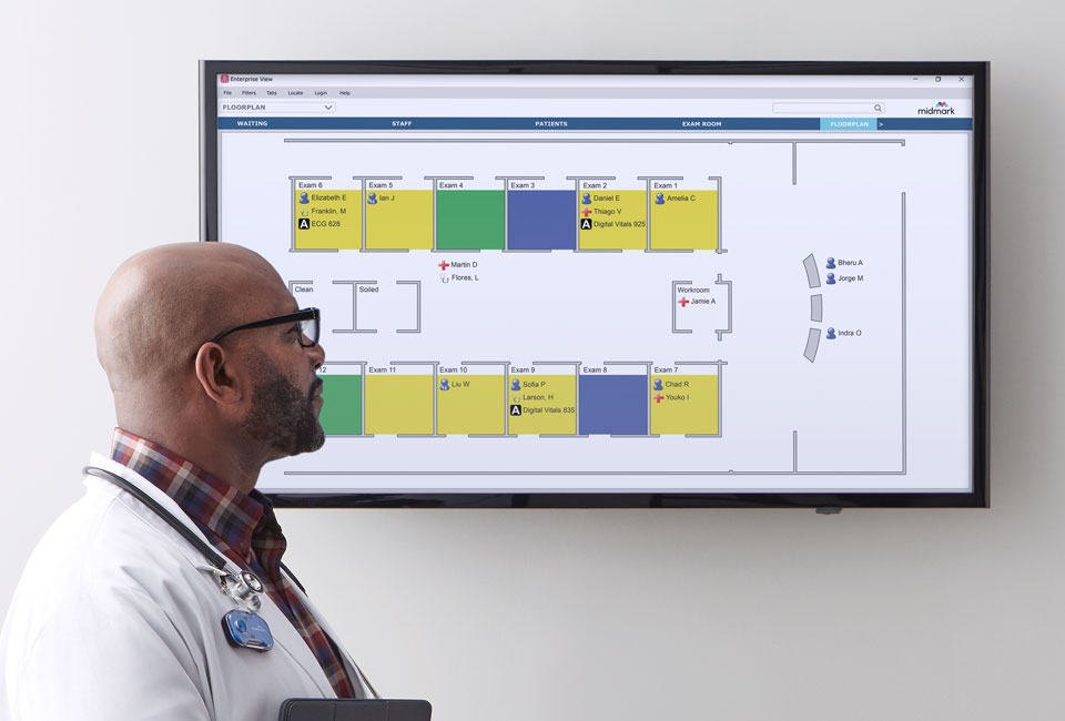 Doctor looking at a screen, depicting a floor layout of exam rooms and their patients