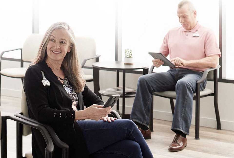 Patients in a waiting room completing information on phones and tablet devices