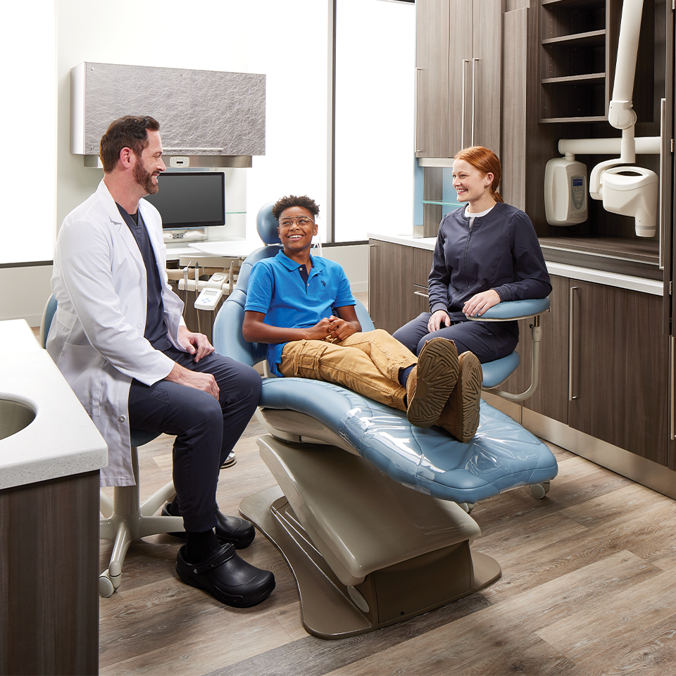 Young male speaking with dentist and dental assistant in Midmark operatory