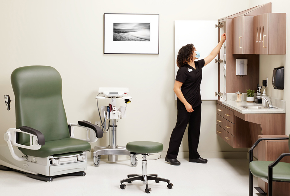 Medical staff in exam room opening cabinetry