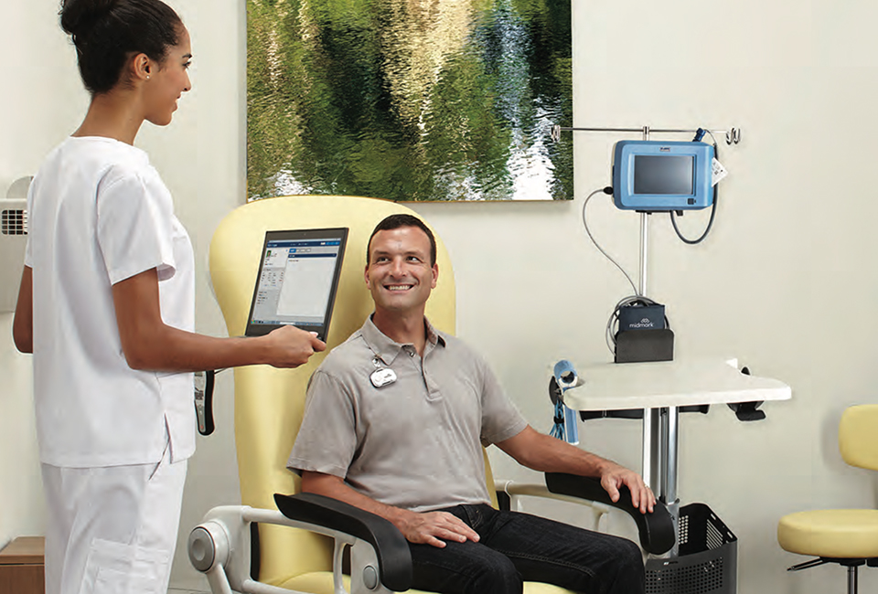 Nurse approaching patient in exam chair with laptop