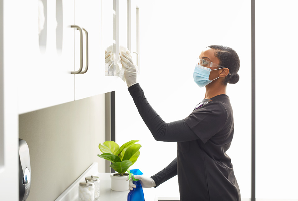 Staff sanitizing and wiping down cabinetry surfaces in an exam room