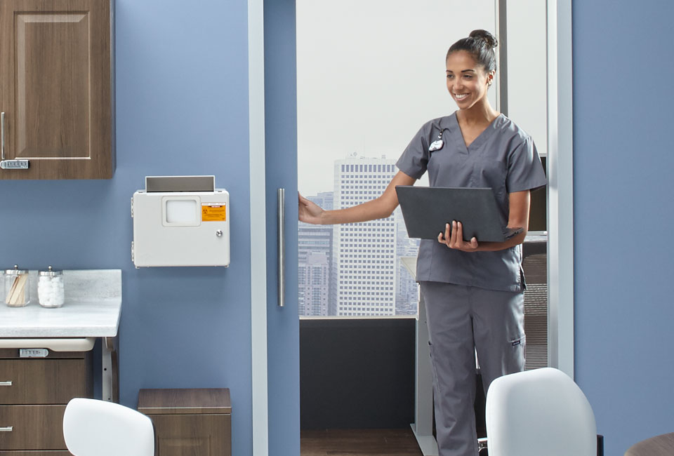 Nurse approaching an exam room with a laptop in hand