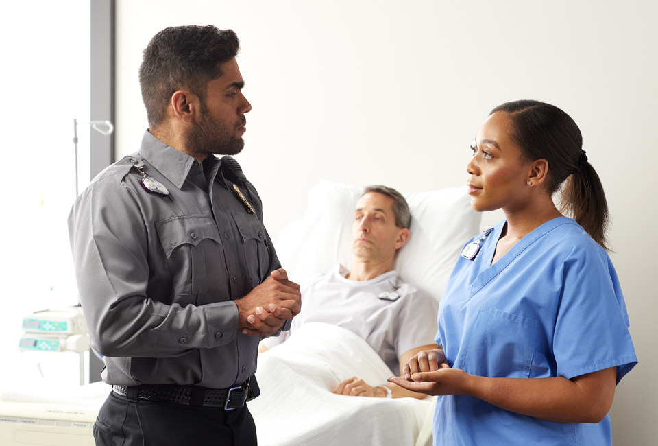 Security staff consulting with a nurse in front of a patient.