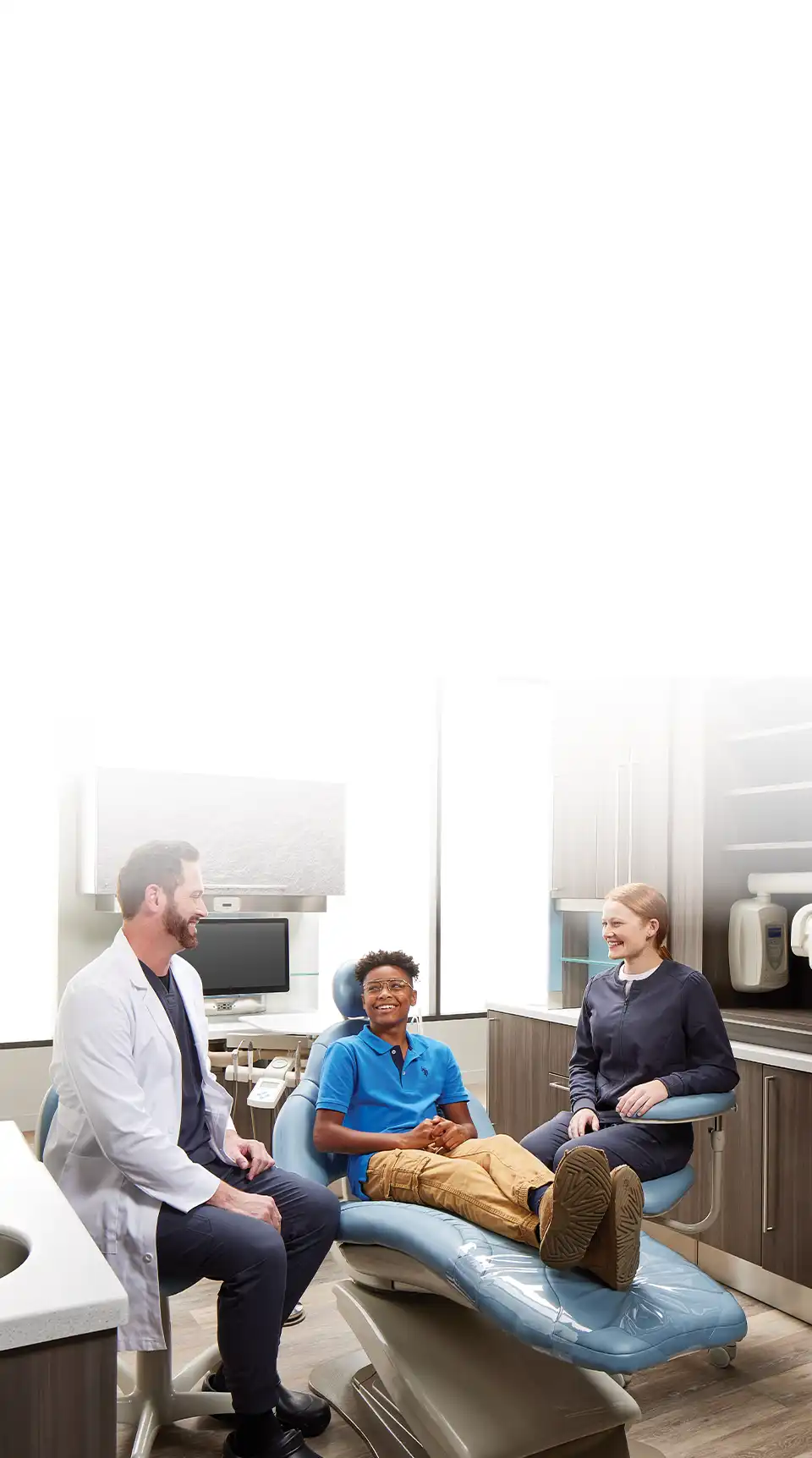 Young male dental patient speaking with dentist and dental assistant in operatory